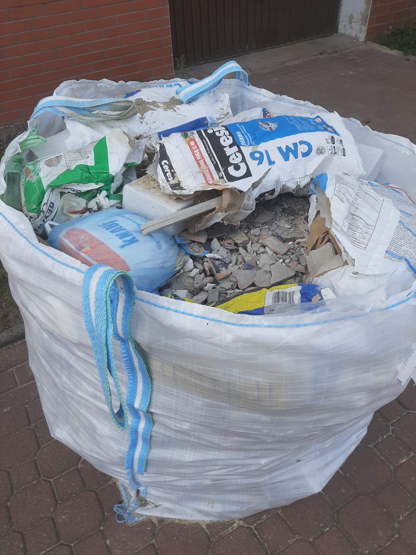 Big bag wypełniony gruzem, workami po zaprawie i opakowaniami budowlanymi