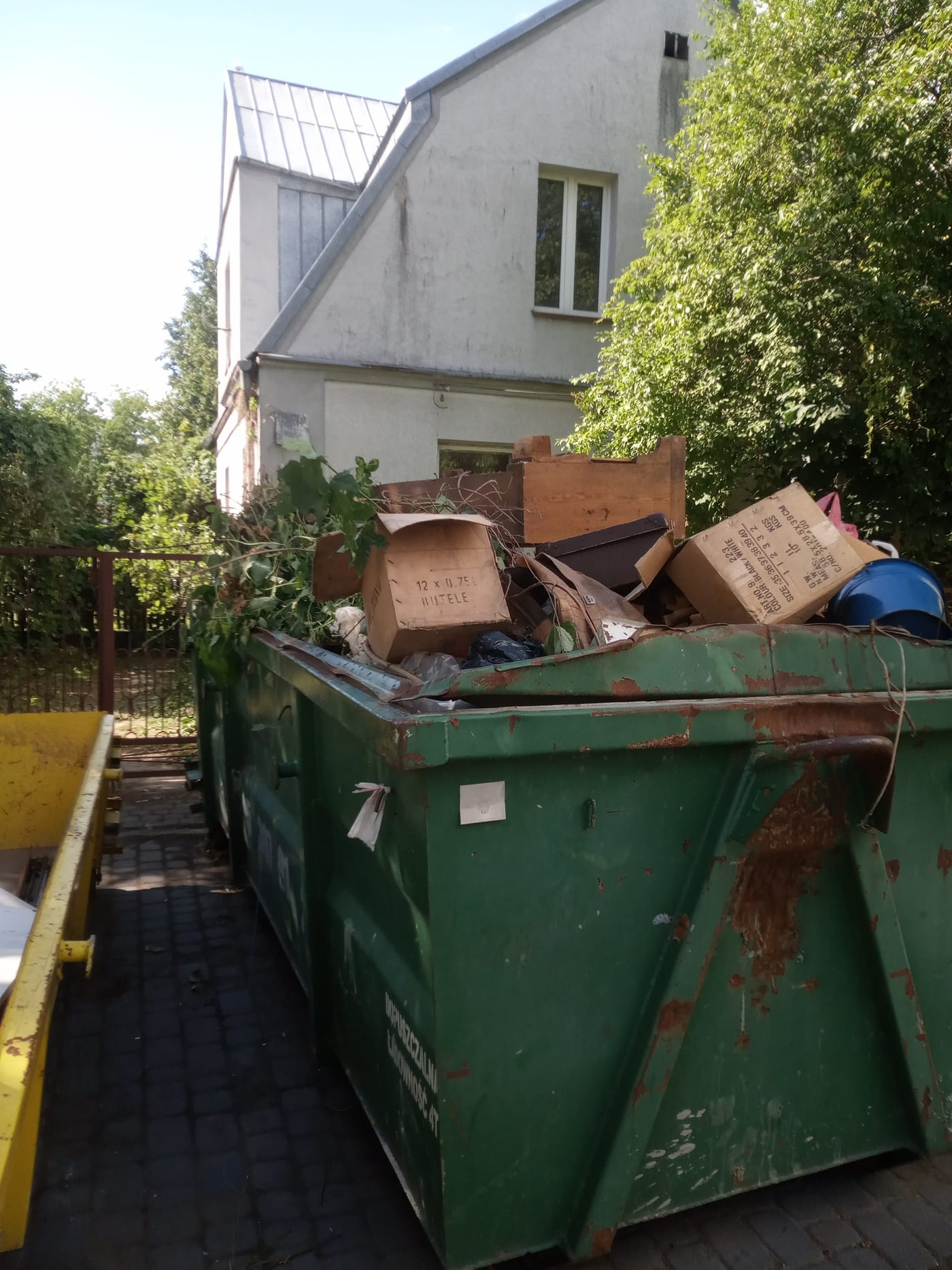 Kontener wypełniony meblami, kartonami i odpadami zielonymi przed domem